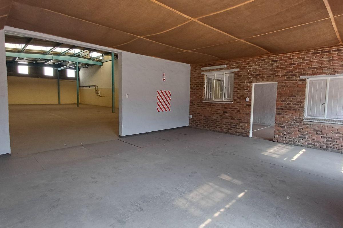 Spacious industrial open-plan area featuring exposed brick walls, concrete flooring, and high-clearance steel roof trusses, suitable for warehouse or workshop use.