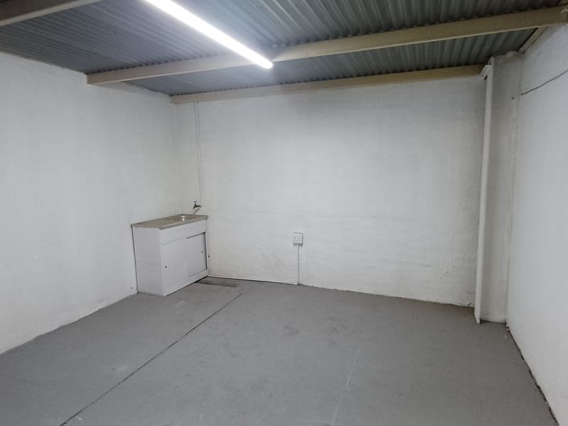 A functional utility space featuring a basic sink, exposed corrugated metal ceiling, and painted concrete flooring, suitable for storage or workshop use.