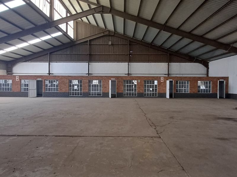 Spacious industrial warehouse featuring high ceilings with exposed steel trusses, skylights, concrete flooring, and a row of integrated brick-built office units.