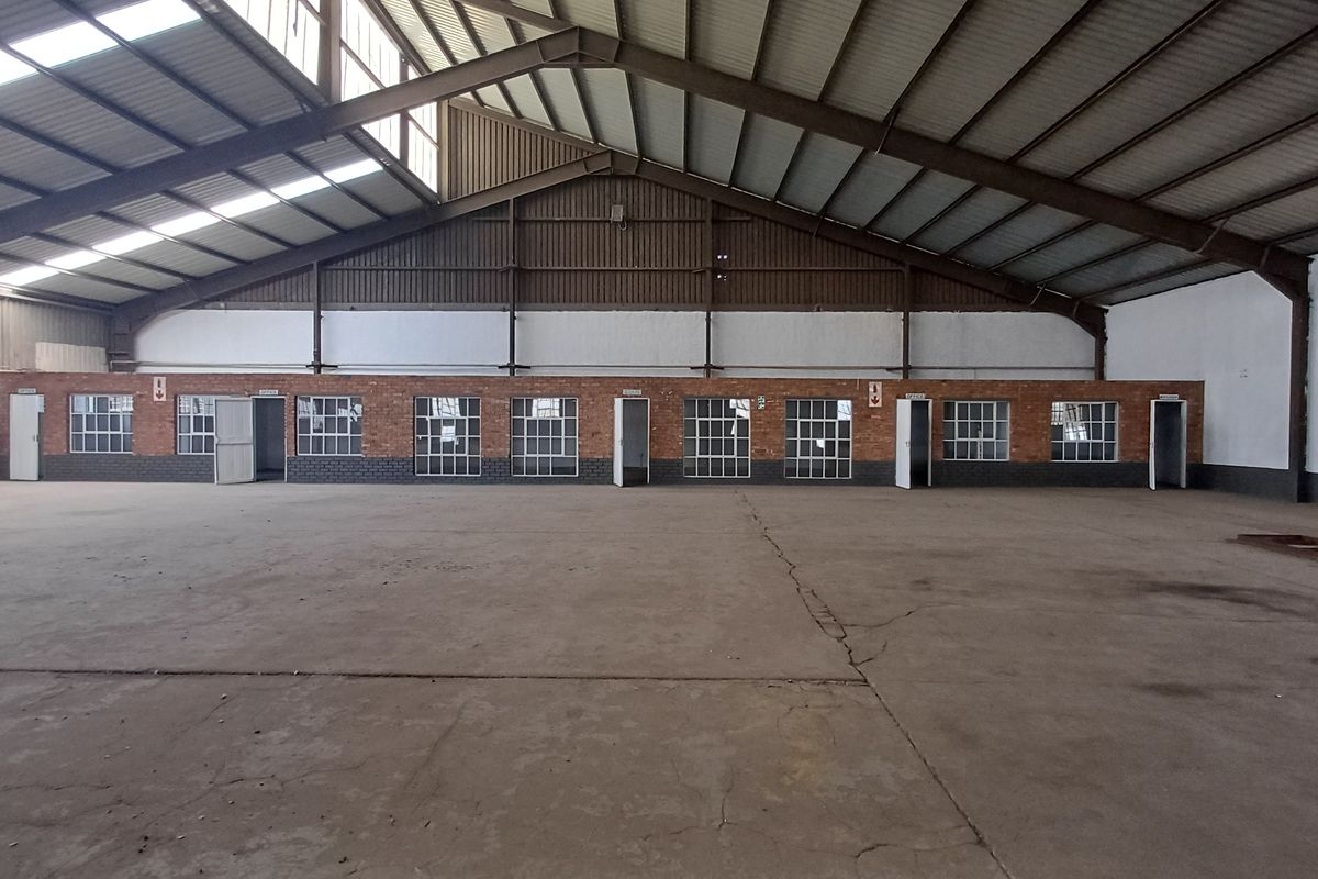 Spacious industrial warehouse featuring high ceilings with exposed steel trusses, skylights, concrete flooring, and a row of integrated brick-built office units.