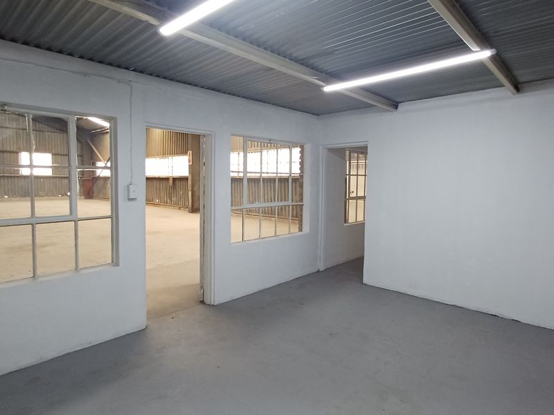 An empty, functional office space featuring painted concrete floors, steel-framed windows, and industrial-style corrugated metal ceiling with strip lighting.