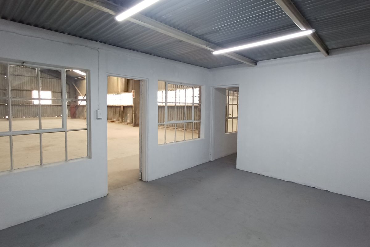 An empty, functional office space featuring painted concrete floors, steel-framed windows, and industrial-style corrugated metal ceiling with strip lighting.