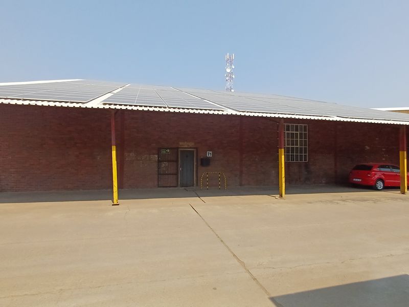 Industrial building exterior featuring a large concrete apron, brick facade, and extensive roof-mounted solar panel array.