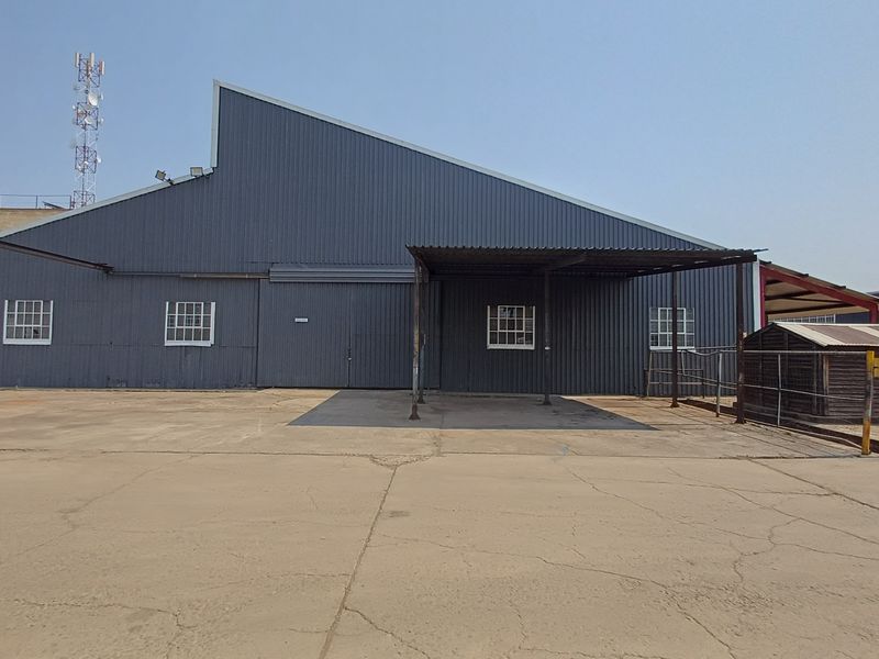 Rear view of an industrial warehouse featuring corrugated metal cladding, a covered loading area, and a large concrete yard with visible surface cracking.