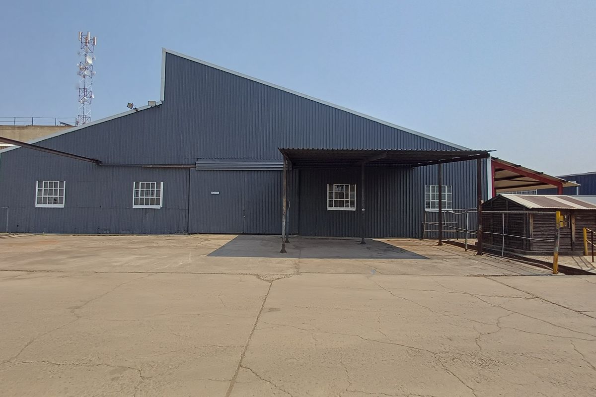 Rear view of an industrial warehouse featuring corrugated metal cladding, a covered loading area, and a large concrete yard with visible surface cracking.
