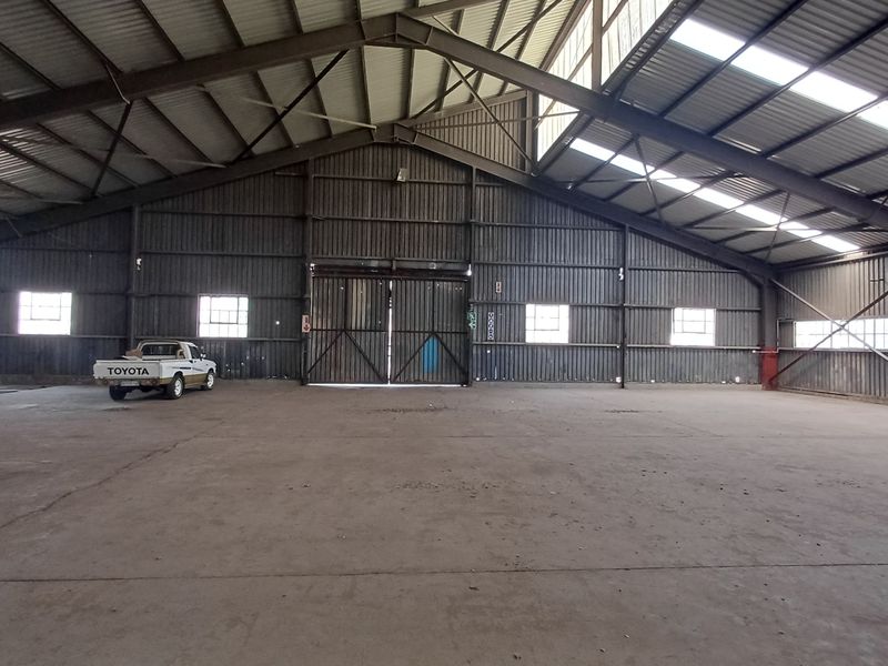 Spacious industrial warehouse featuring a high-clearance steel portal frame, concrete flooring, natural light through skylights, and large sliding access doors.