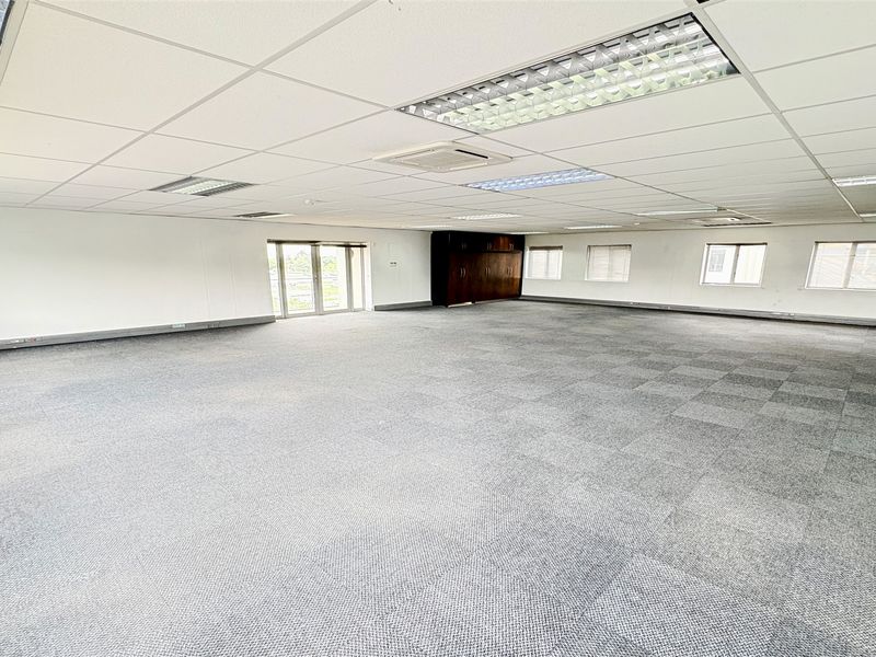 A spacious, open-plan office area featuring carpet tiles, suspended ceilings with recessed lighting, built-in storage cabinetry, and ducted air conditioning.