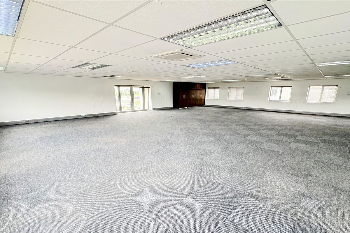 A spacious, open-plan office area featuring carpet tiles, suspended ceilings with recessed lighting, built-in storage cabinetry, and ducted air conditioning.