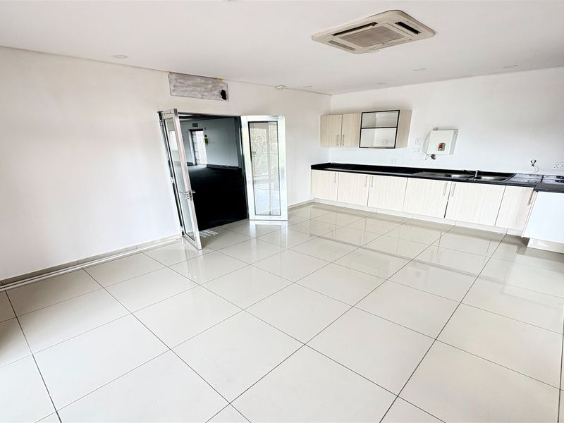 Spacious open-plan office area featuring a kitchenette with built-in cabinetry, black granite countertops, tiled flooring, and integrated ceiling air conditioning.