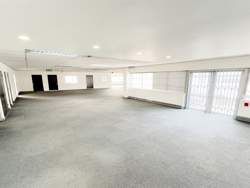 A spacious, open-plan office area featuring neutral carpet tiles, recessed lighting, and a secure sliding glass door leading to an exterior balcony.