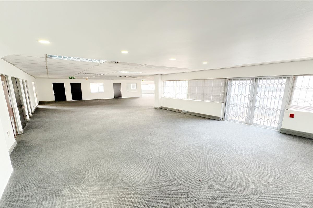A spacious, open-plan office area featuring neutral carpet tiles, recessed lighting, and a secure sliding glass door leading to an exterior balcony.