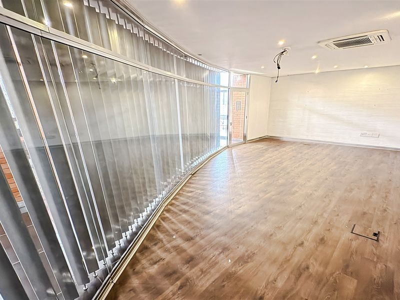 A bright, empty office space featuring curved glass partitioning, modern laminate flooring, recessed lighting, and integrated ducted air conditioning.