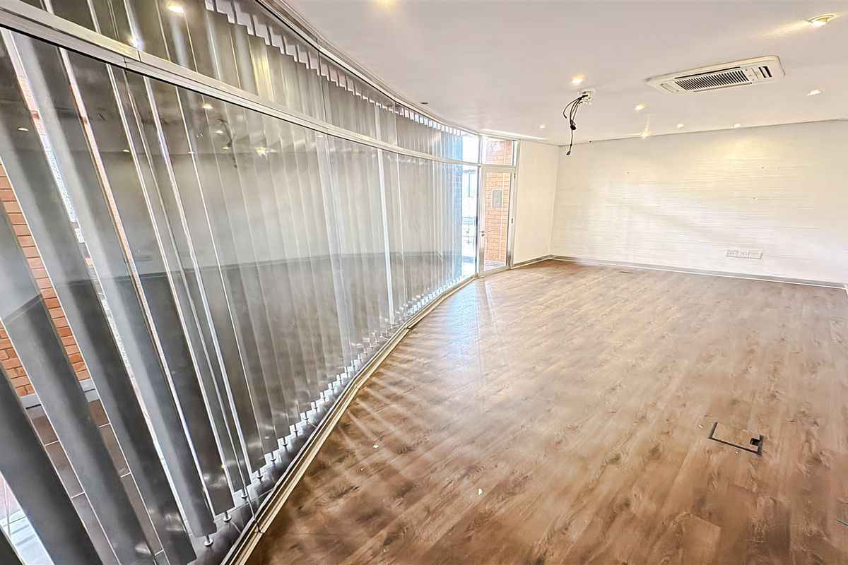 A bright, empty office space featuring curved glass partitioning, modern laminate flooring, recessed lighting, and integrated ducted air conditioning.
