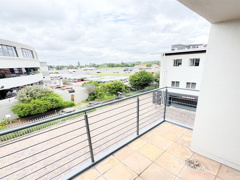 A clean, open-air balcony featuring tiled flooring, a metal safety balustrade, and a view overlooking the surrounding office park and parking area.