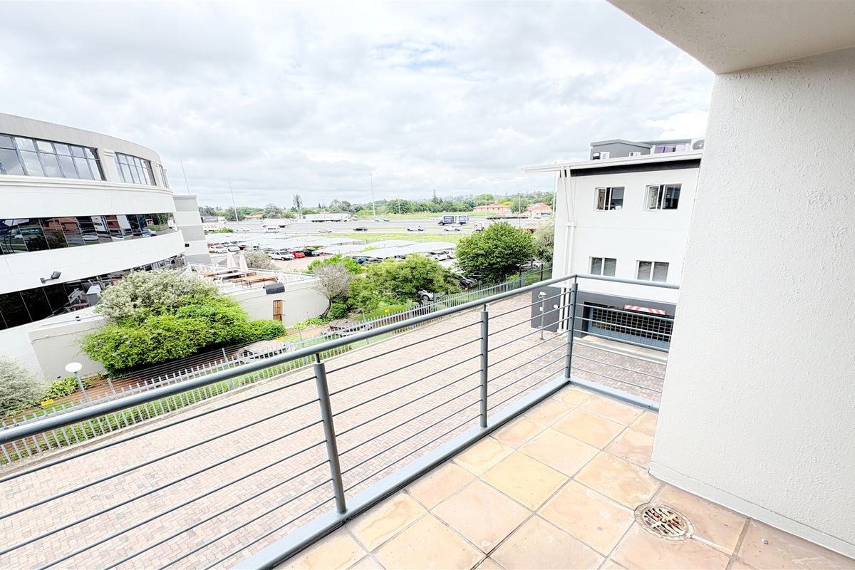 A clean, open-air balcony featuring tiled flooring, a metal safety balustrade, and a view overlooking the surrounding office park and parking area.