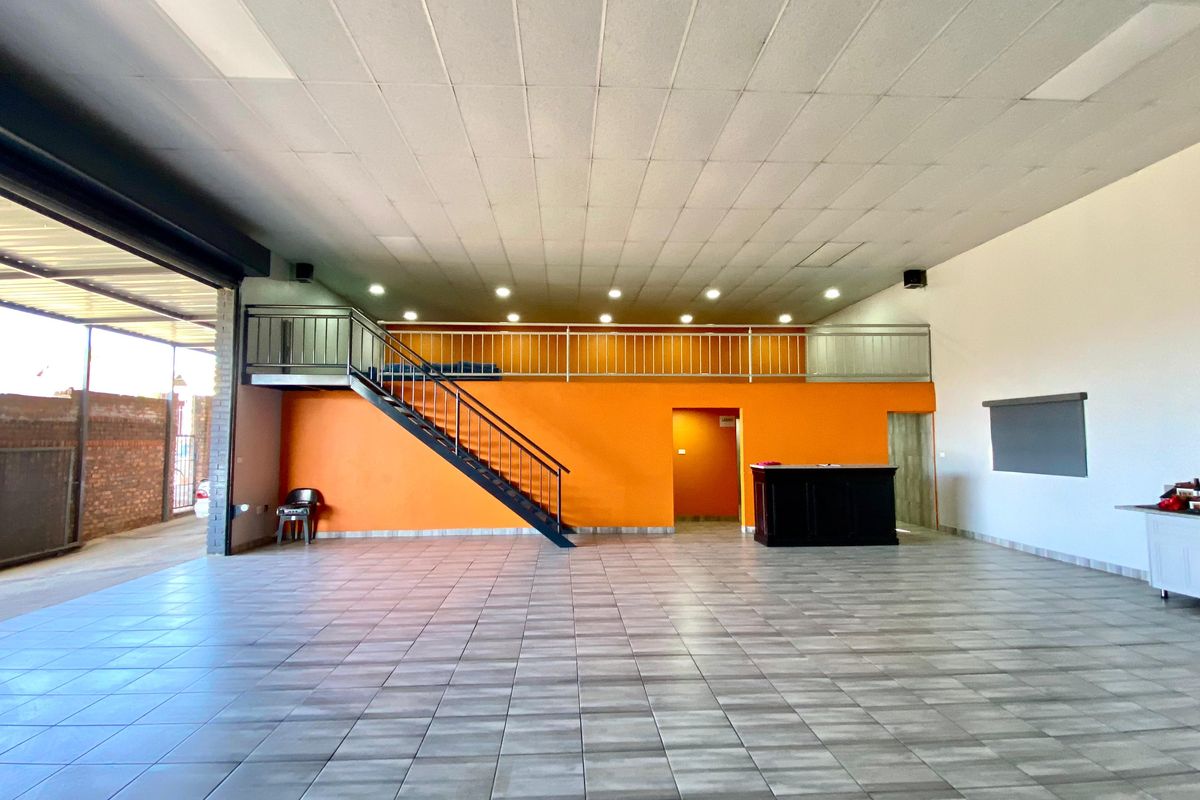 Spacious open-plan commercial area featuring a mezzanine level, metal staircase, tiled flooring, and built-in cabinetry, suitable for various business applications.