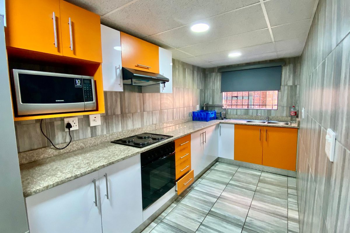 Modern kitchen featuring vibrant orange and white cabinetry, granite countertops, integrated oven and hob, and tiled finishes throughout.