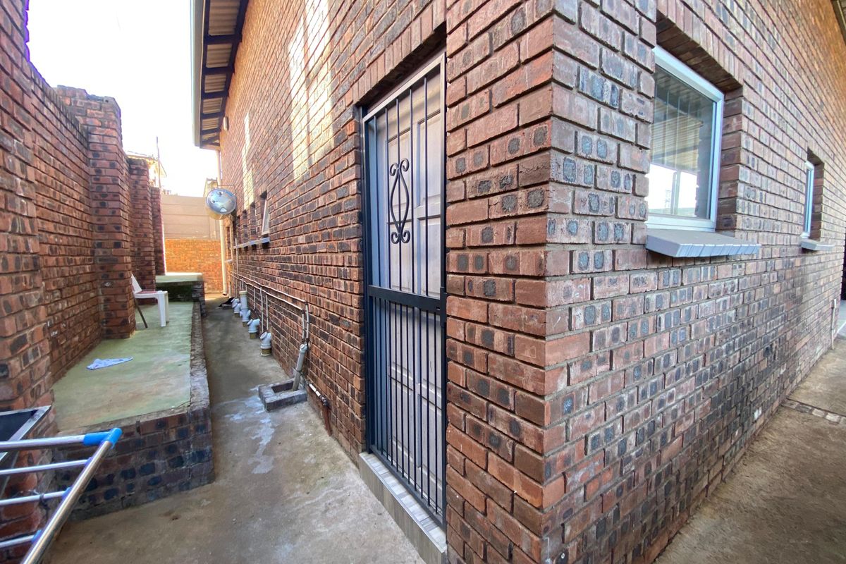 A side view of the commercial property featuring face brick exterior walls, a secure metal gate, and a concrete pathway with external plumbing fixtures.