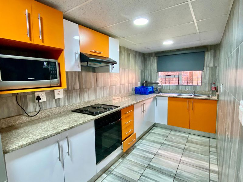 Modern kitchen featuring vibrant orange and white cabinetry, granite countertops, integrated oven and hob, and tiled finishes throughout.