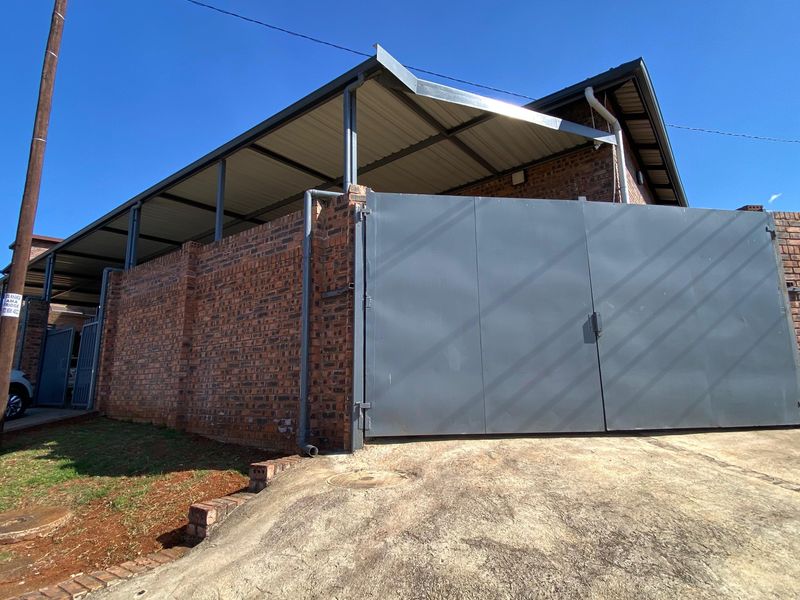 Commercial property exterior featuring a secure gated entrance, face brick boundary wall, and a covered carport area with a concrete driveway.