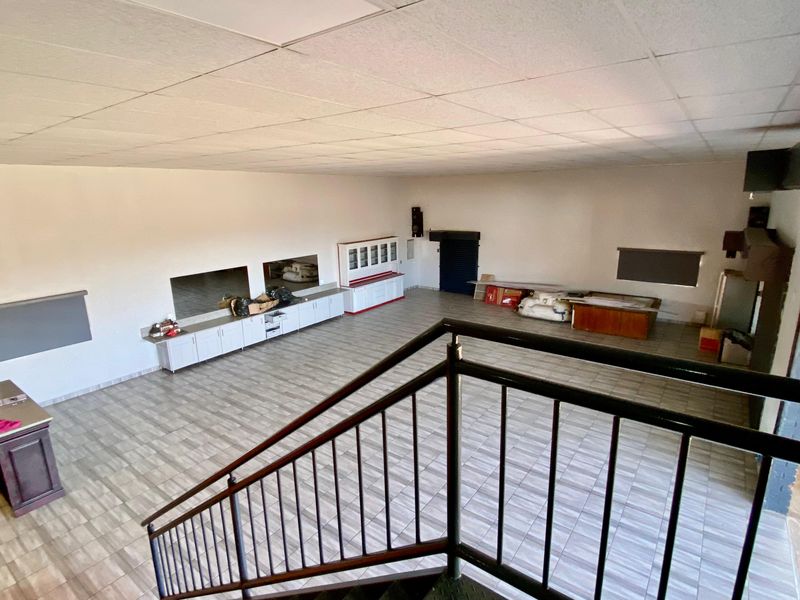 Spacious open-plan commercial area featuring tiled flooring, built-in cabinetry, and a suspended ceiling, accessible via an internal staircase.