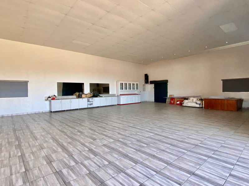A spacious, open-plan commercial area featuring tiled flooring, a suspended ceiling, and built-in cabinetry, suitable for various business or retail applications.
