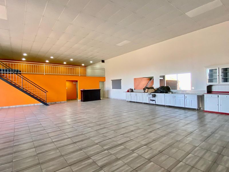 Spacious open-plan commercial area featuring a mezzanine level, metal staircase, tiled flooring, and built-in cabinetry along the wall.