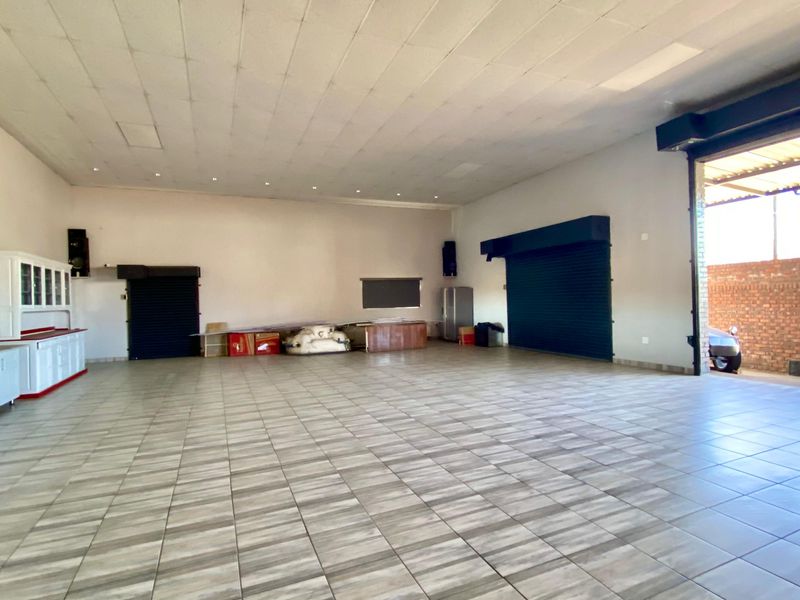 Spacious open-plan commercial area featuring tiled flooring, suspended ceilings, and multiple roller shutter doors, suitable for various business or retail applications.