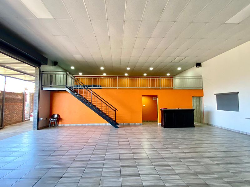 Spacious open-plan commercial area featuring a mezzanine level, metal staircase, tiled flooring, and built-in cabinetry, suitable for various business applications.