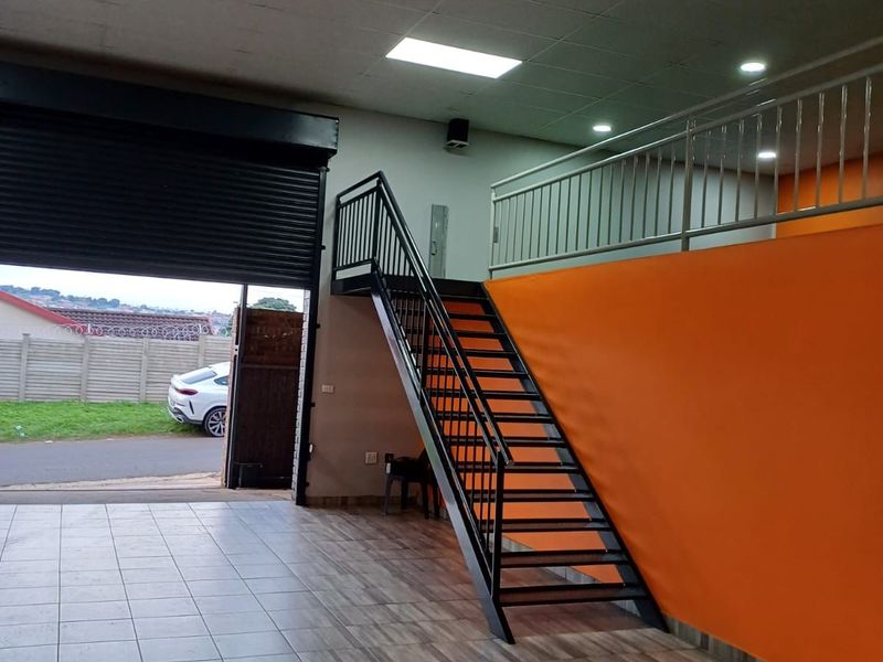 Commercial utility space featuring a roller shutter door, tiled flooring, and a metal staircase leading to a mezzanine level with a safety balustrade.