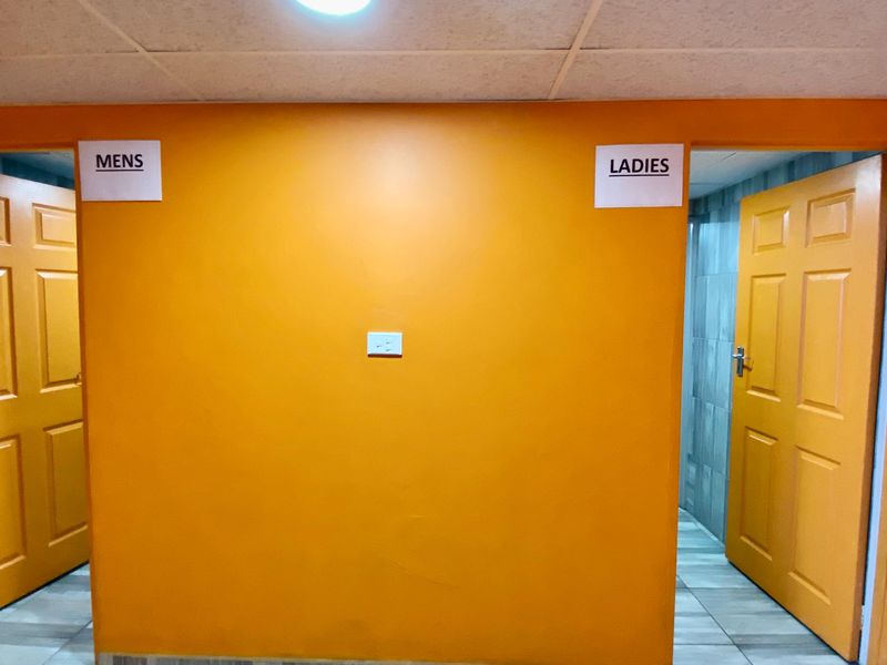 A commercial hallway featuring orange painted walls, tiled flooring, and separate access points for men's and ladies' restrooms.
