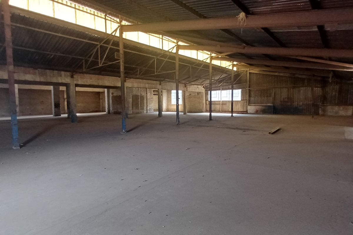 Expansive industrial warehouse space featuring high ceilings with exposed steel trusses, concrete flooring, and ample natural light from clerestory windows.