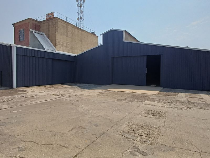 Industrial warehouse exterior featuring dark blue corrugated metal cladding, large sliding access doors, and an expansive concrete yard area.
