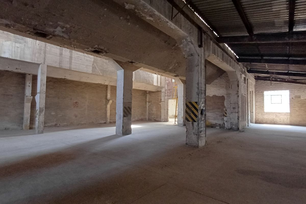 Expansive industrial utility space featuring high ceilings, exposed structural concrete columns, and durable concrete flooring, suitable for warehouse or workshop conversion.