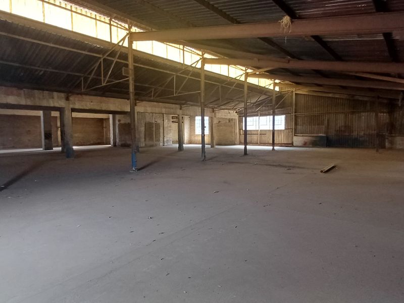 Expansive industrial warehouse space featuring high ceilings with exposed steel trusses, concrete flooring, and ample natural light from clerestory windows.