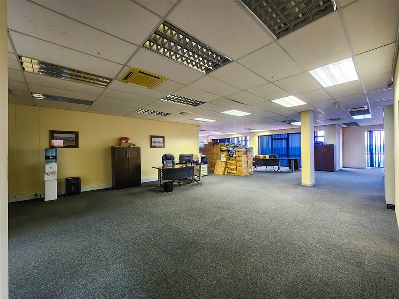 Spacious open-plan office area featuring a suspended ceiling with recessed lighting, carpeted flooring, and a central structural column.
