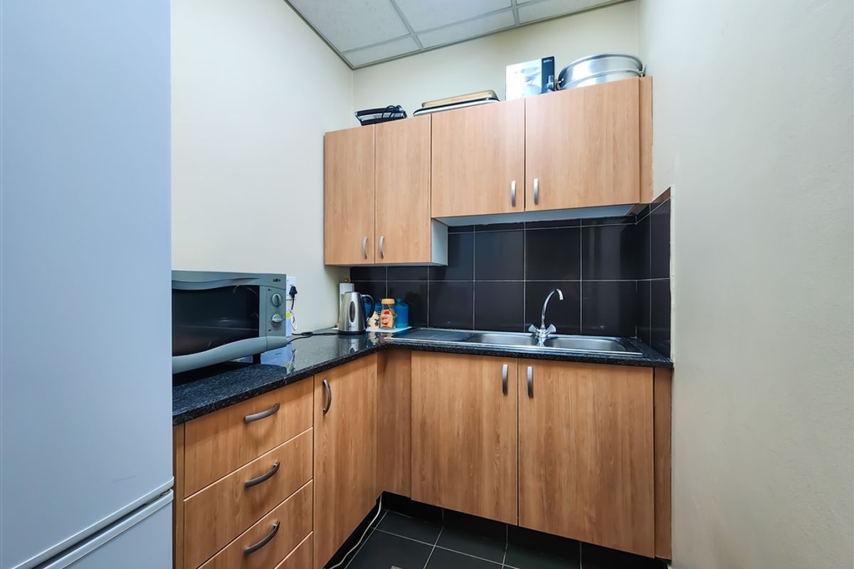 A compact office kitchenette featuring laminate cabinetry, granite countertops, a stainless steel sink, and dark tiled flooring.