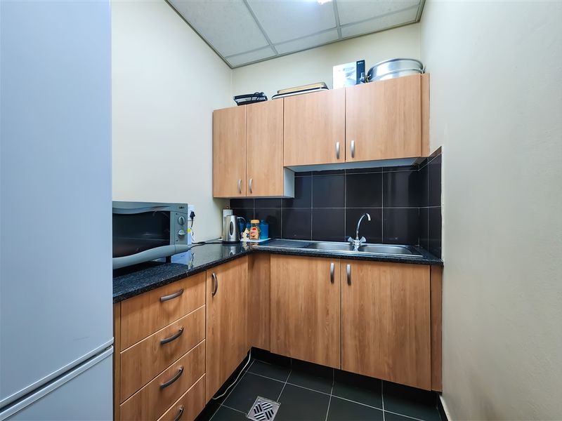 A compact office kitchenette featuring laminate cabinetry, granite countertops, a stainless steel sink, and dark tiled flooring.