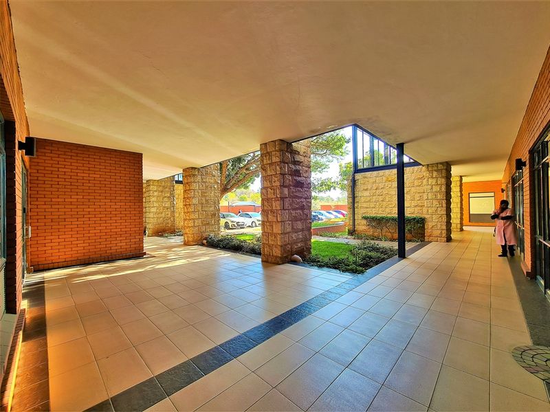 A spacious, covered outdoor walkway featuring stone-clad columns, tiled flooring, and a clean, modern architectural design connecting office building sections.