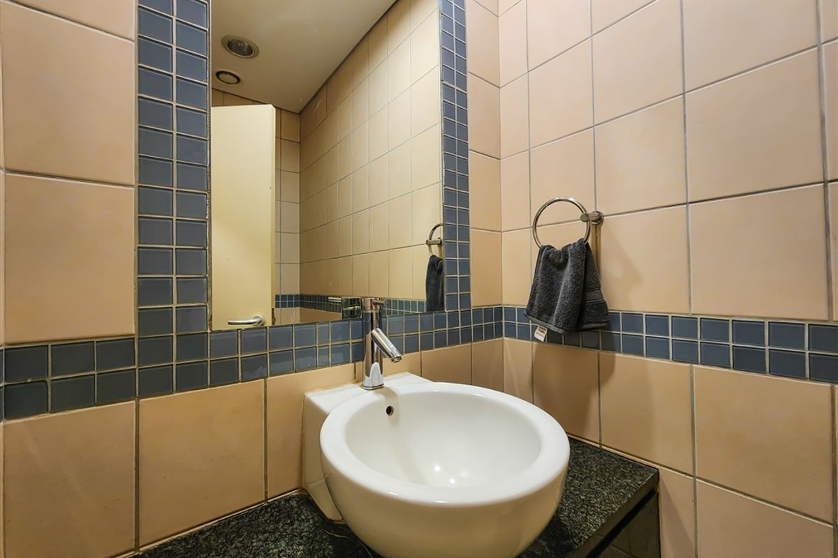A compact office bathroom featuring a wall-mounted basin, granite vanity top, and decorative tiled wall finishes.