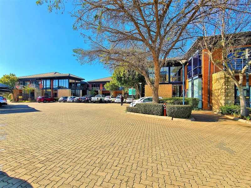 A well-maintained office park exterior featuring brick and stone facade, large glass windows, and an expansive paved parking area.
