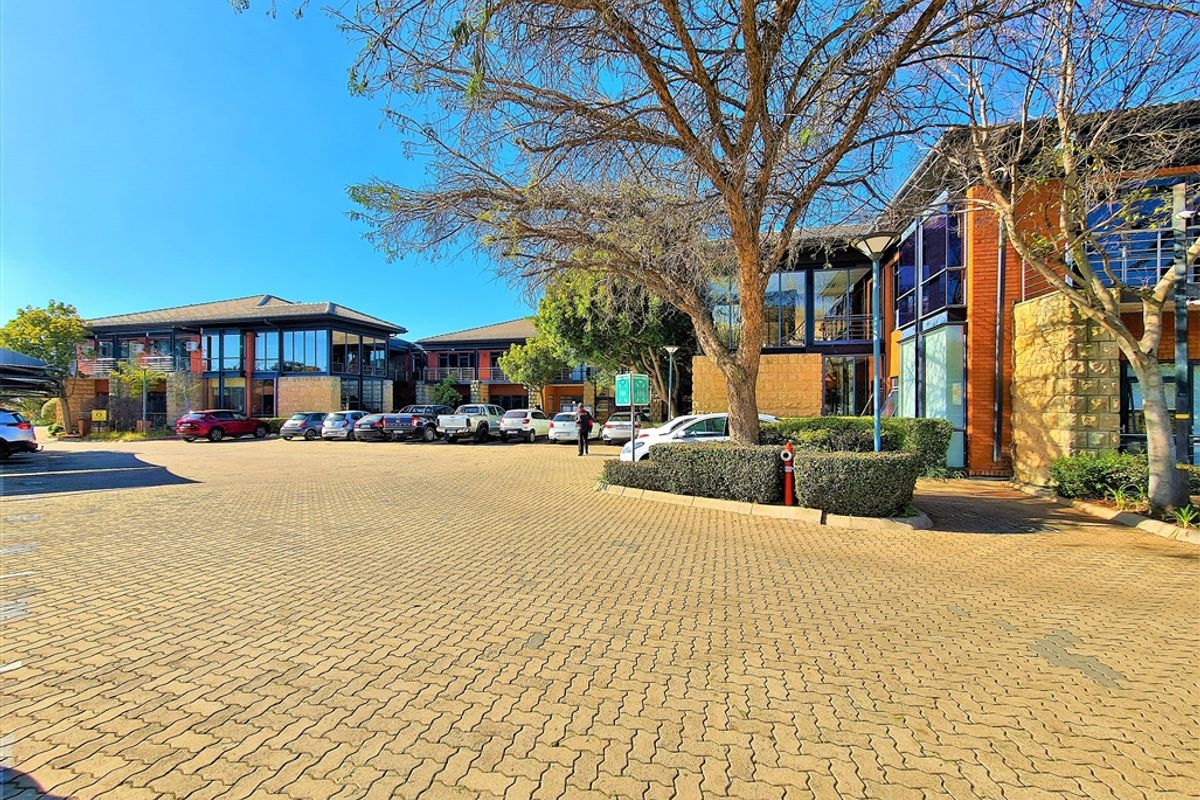 A well-maintained office park exterior featuring brick and stone facade, large glass windows, and an expansive paved parking area.