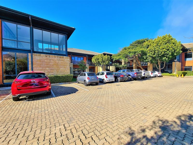 Exterior view of a modern office building featuring stone cladding, large glass windows, and a paved parking area.