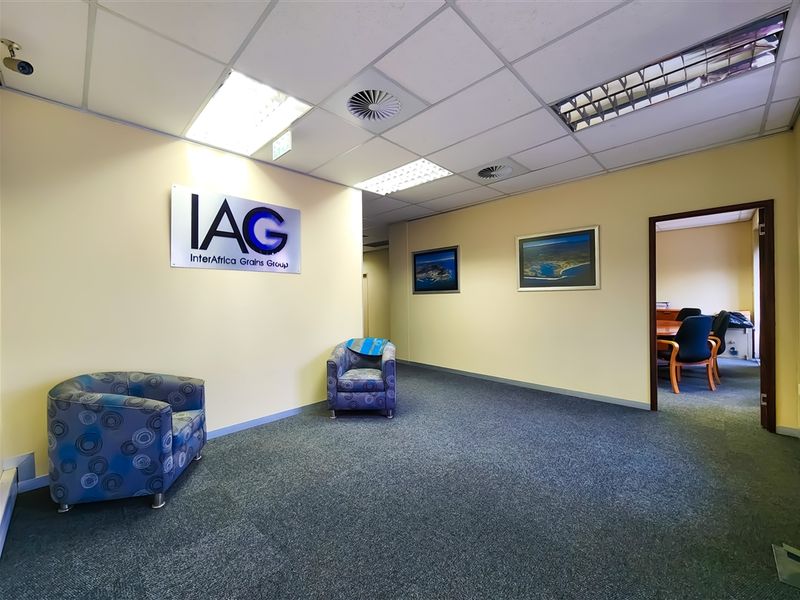 A professional office reception area featuring carpeted flooring, a suspended ceiling with integrated lighting, and access to an adjoining office space.
