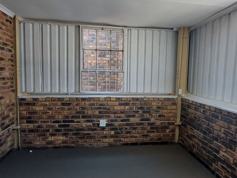 An empty office space featuring exposed brick walls, corrugated metal cladding, and security-barred windows, offering a functional industrial-style workspace.