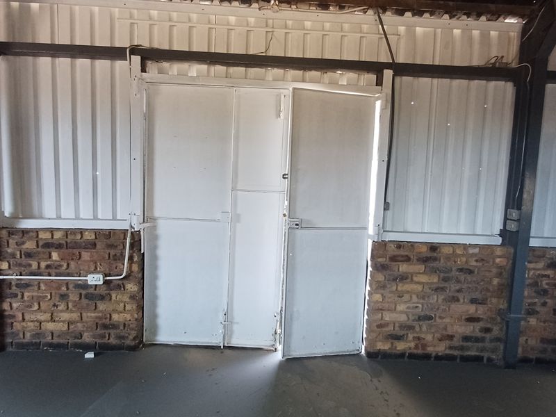 An industrial-style office space featuring exposed brickwork, corrugated metal wall cladding, and steel structural elements with double metal access doors.
