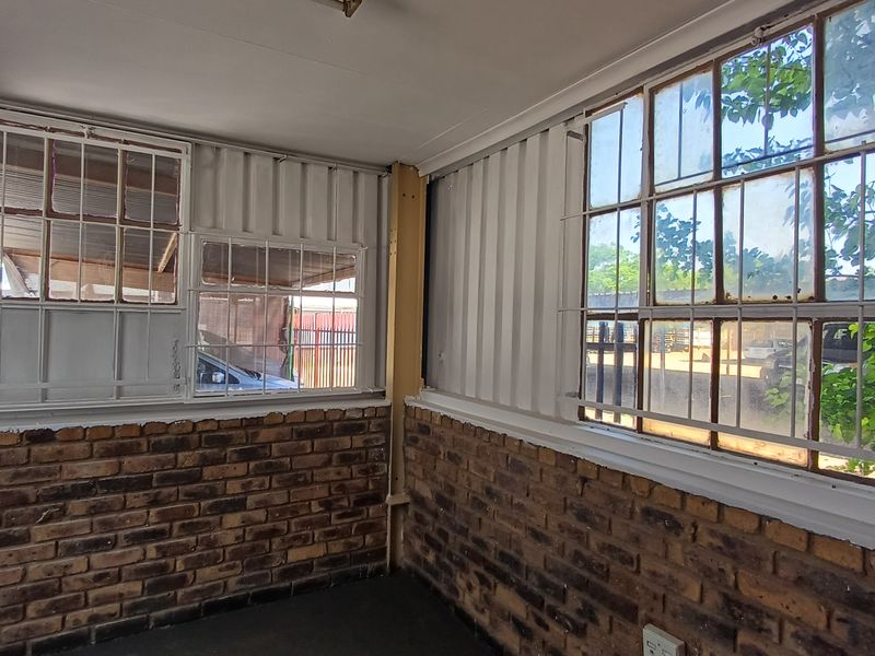 An empty office space featuring exposed brickwork, corrugated metal wall cladding, and large steel-framed windows with security bars.