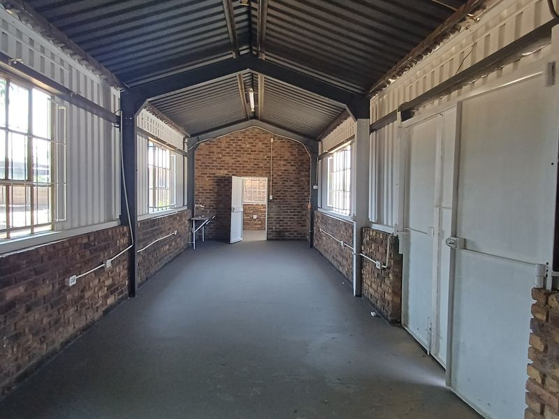 Spacious industrial-style office area featuring exposed brick walls, steel structural framing, concrete flooring, and large windows providing ample natural light.