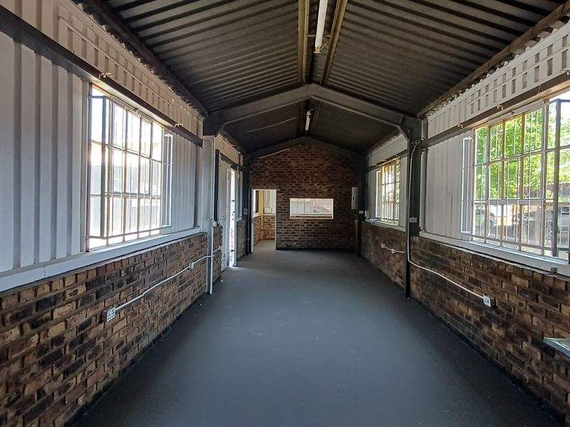 An empty, industrial-style office space featuring exposed brick walls, steel-framed windows, and a high corrugated metal ceiling with exposed structural beams.