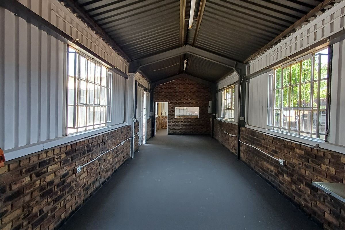 An empty, industrial-style office space featuring exposed brick walls, steel-framed windows, and a high corrugated metal ceiling with exposed structural beams.